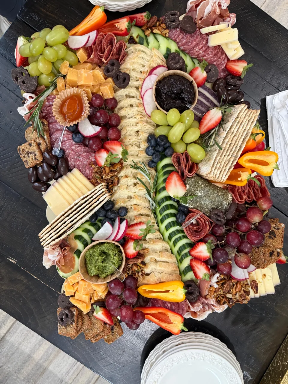 Large grazing board with cured meats, cheeses, bread, crackers, cucumber, grapes, berries, peppers and dips