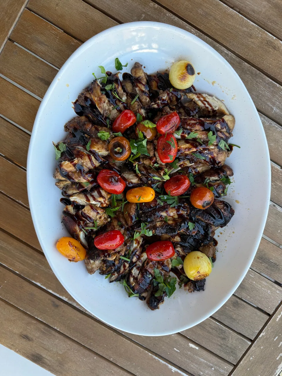 Platter of sliced chicken with blistered tomatoes, balsamic glaze and parsley