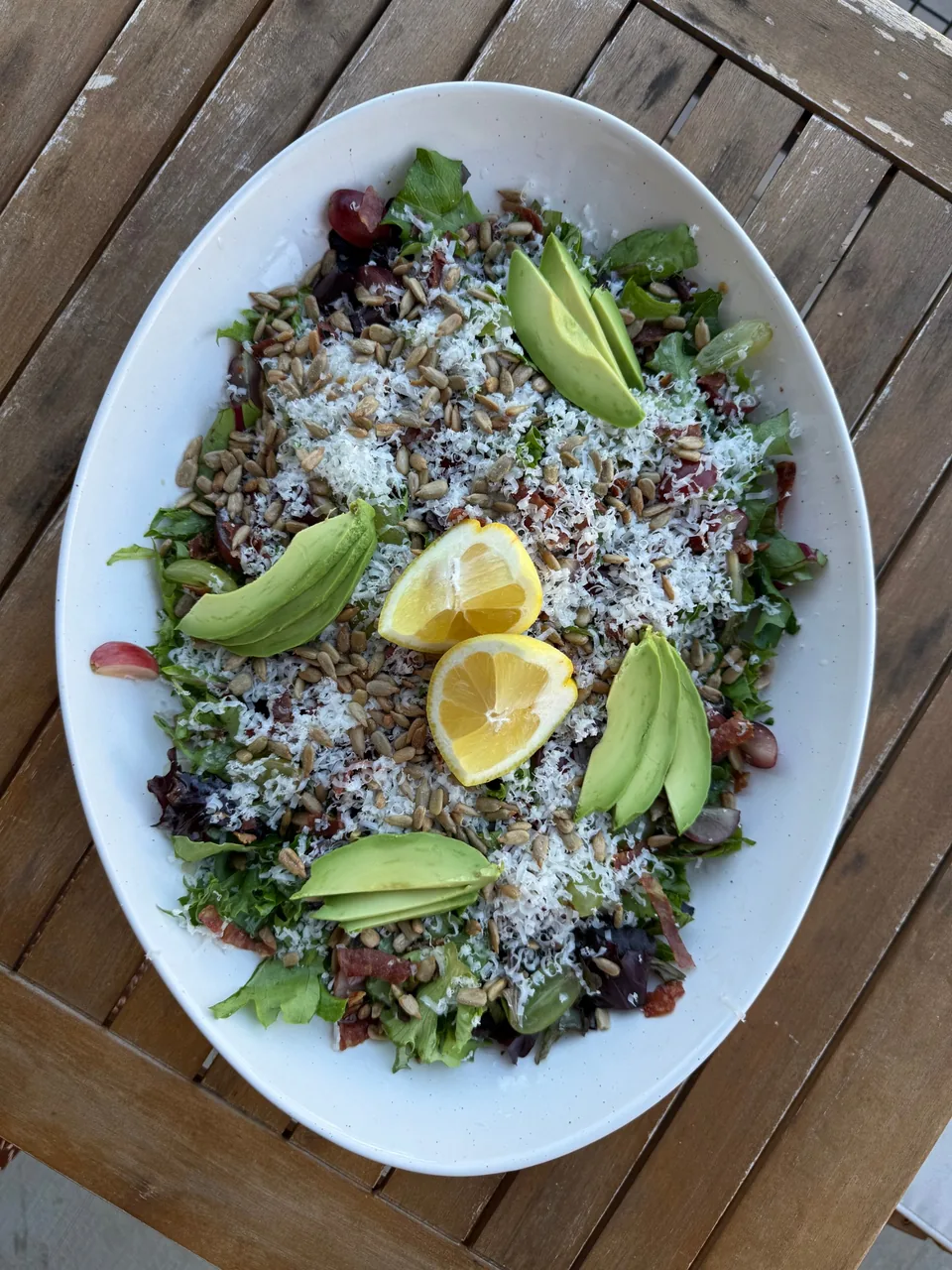 Green salad with sunflower seeds, grated parmesan, sliced avocado and lemon