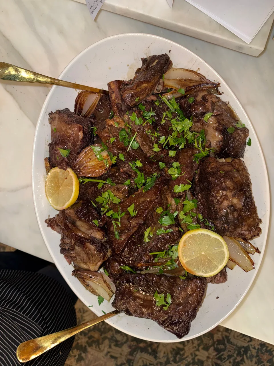 Platter of braised short ribs with roasted shallots, lemon slices and chopped parsley