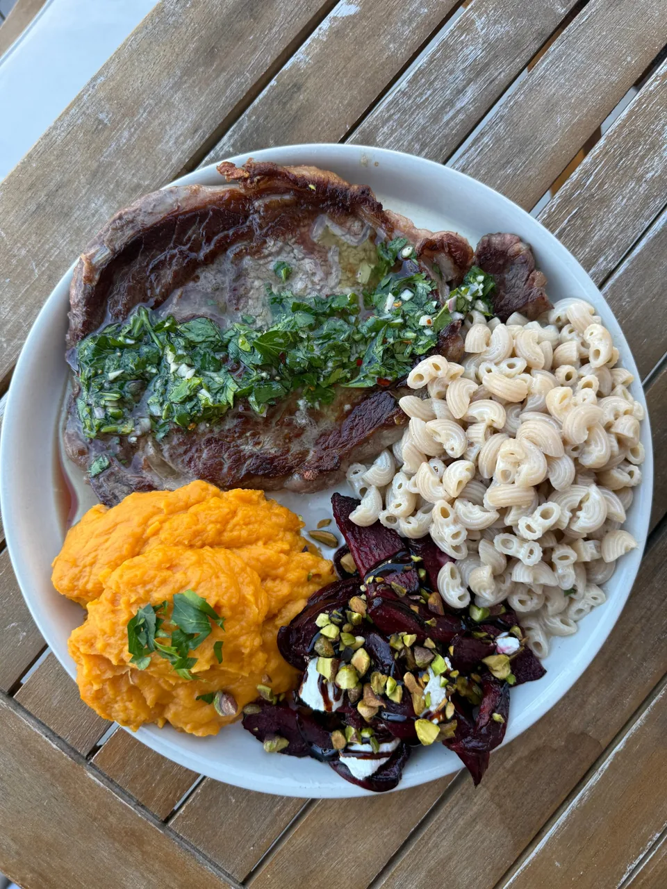 Seared steak topped with chimichurri, with mashed sweet potato, beets with pistachio and pasta