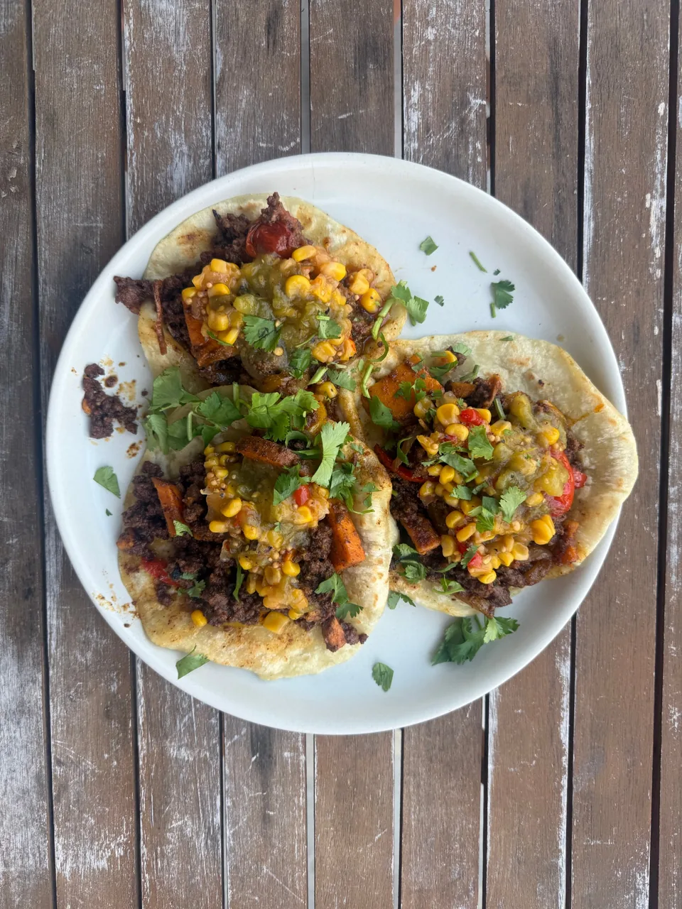 Three tacos with ground beef, sweet potato, charred corn salsa, salsa verde and cilantro